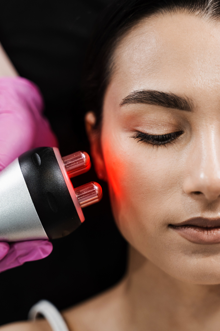 Radio frequency lifting with red light for young woman close-up. Dermatologist is doing radio frequency RF skin tightening. RF facelift firms and lifts sagging skin.